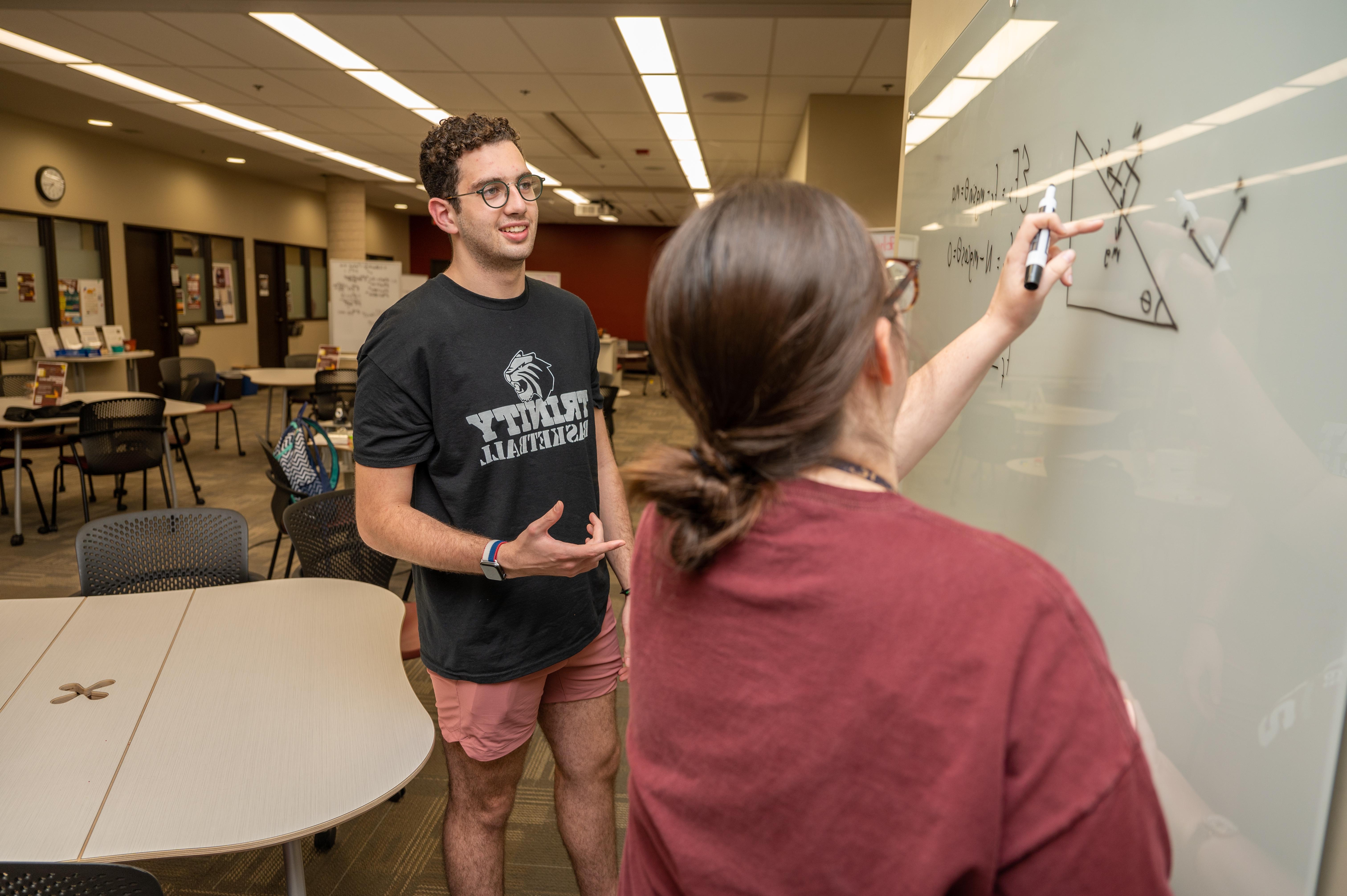 a student and a professor stand in front of a whiteboard during mathematics tutoring