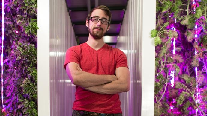 Mitch Hagney stands in his hydroponic system lit by blacklight