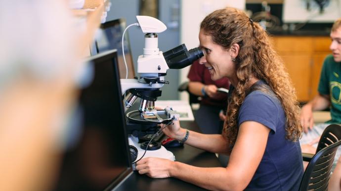 Picture of Kathy Surpless looking through a microscope in a science lab. 