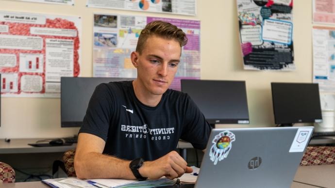 Nathan Brown looks at a laptop in the Storch computer lab, with student academic posters behind him