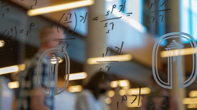 Equations written on the windows of the makerspace; people working in the background