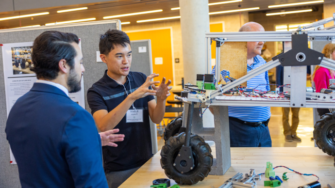 A student explains his engineering project to someone at the Summer Undergraduate Rsearch and Internship Symposium