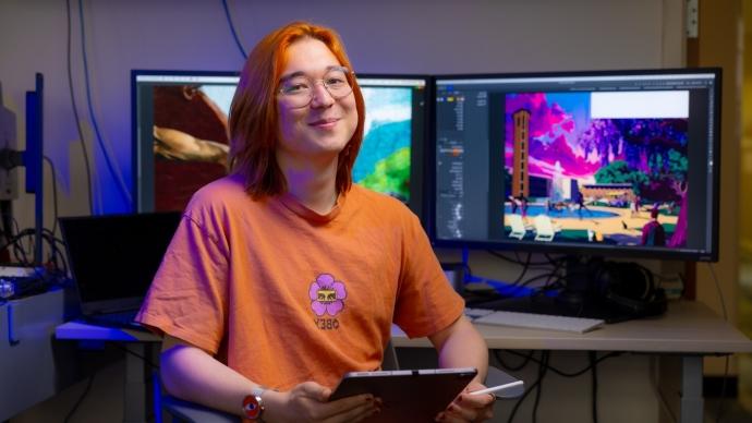 A student with orange hair and clothes sits in front of a computer.