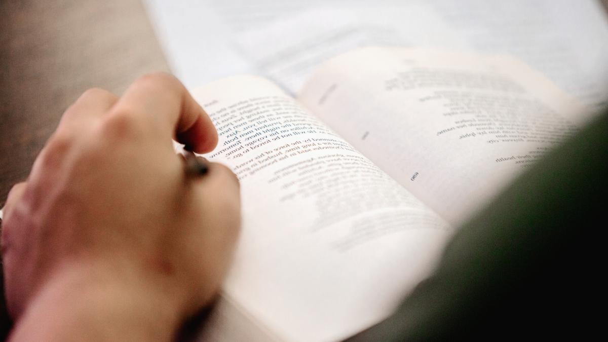 hand holds a pen to an open book