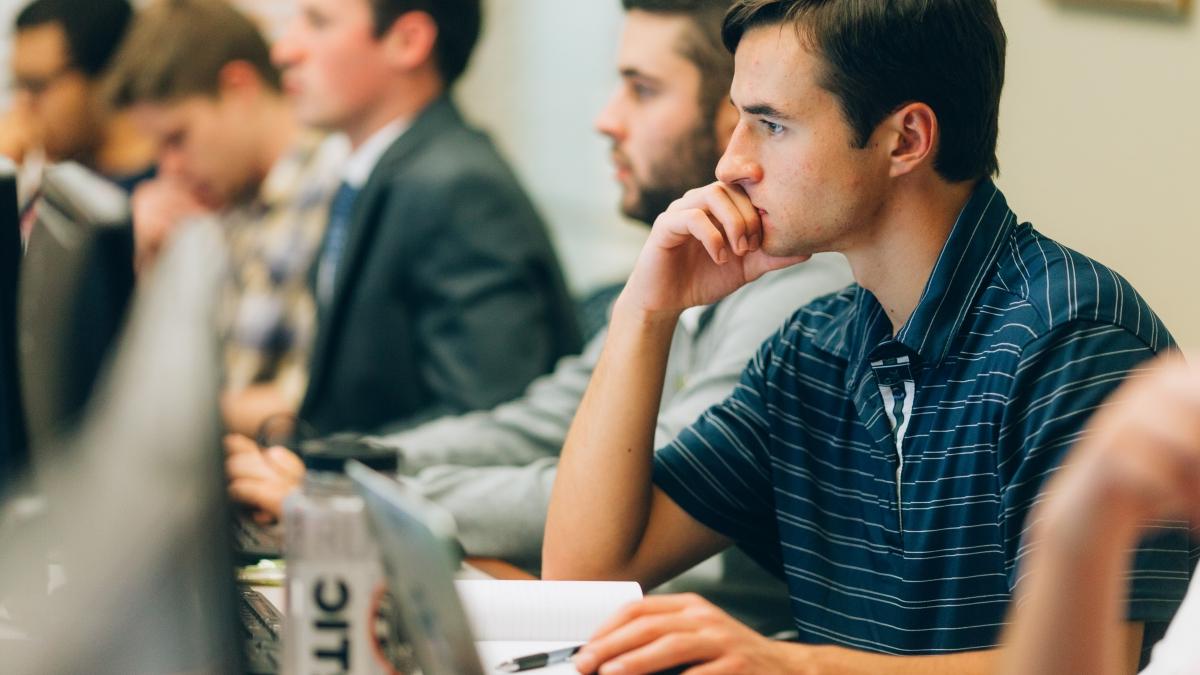 student thinks while working on a computer in a crowded classroom