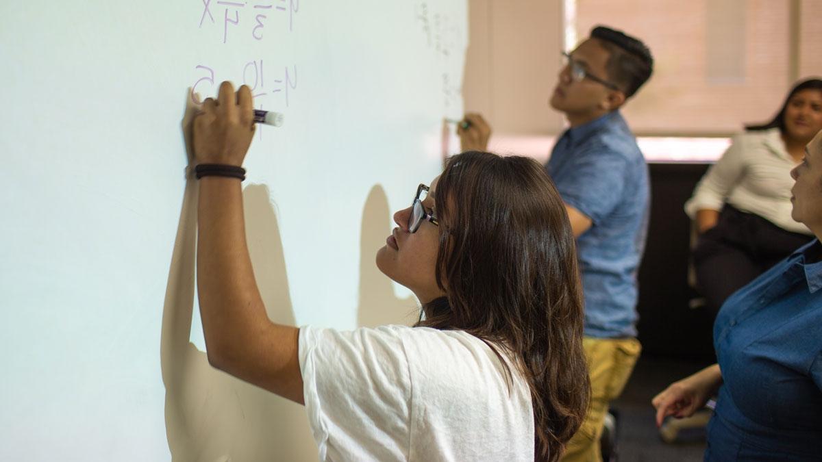 向上的束缚 students Karla Chavez and Victor Casillas writing math on a board.